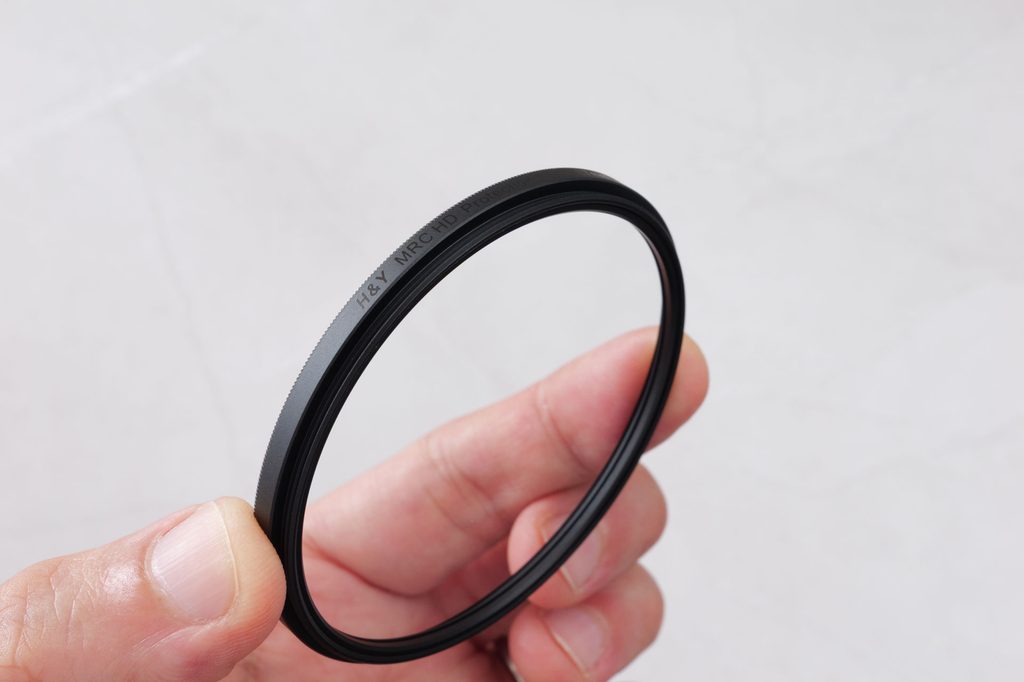 手に持ったH&Y MRC HD Protection Filter 67mm。枠にマットブラックで製品名が印字されている